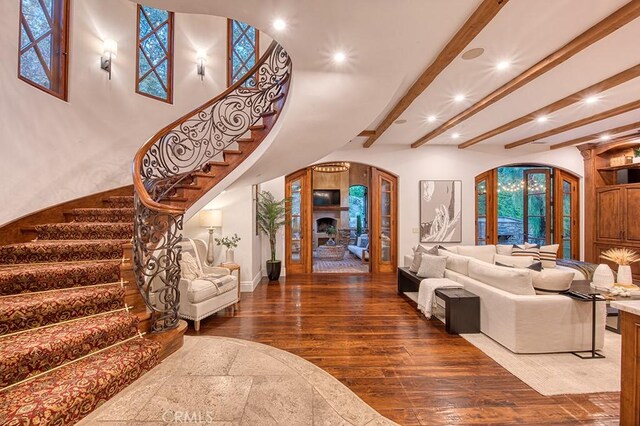 living area featuring recessed lighting, arched walkways, stairs, wood-type flooring, and beamed ceiling