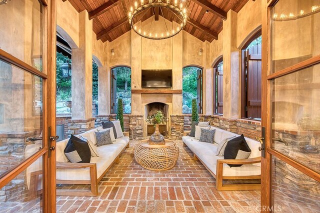 living area with high vaulted ceiling, brick floor, an outdoor fireplace, wooden ceiling, and a chandelier