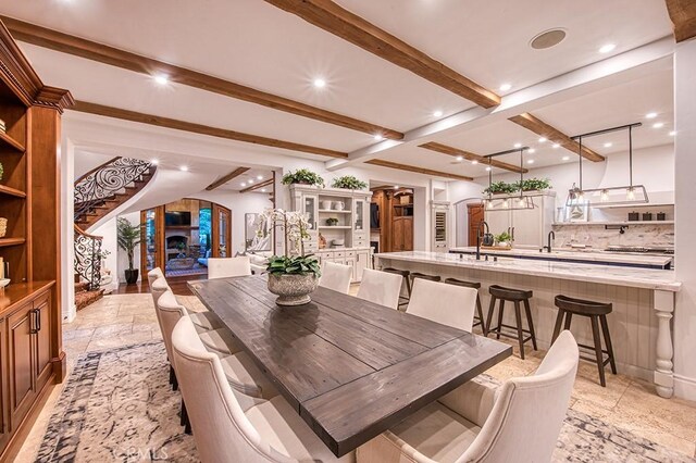 dining space featuring beam ceiling, stairway, a fireplace, and stone tile floors