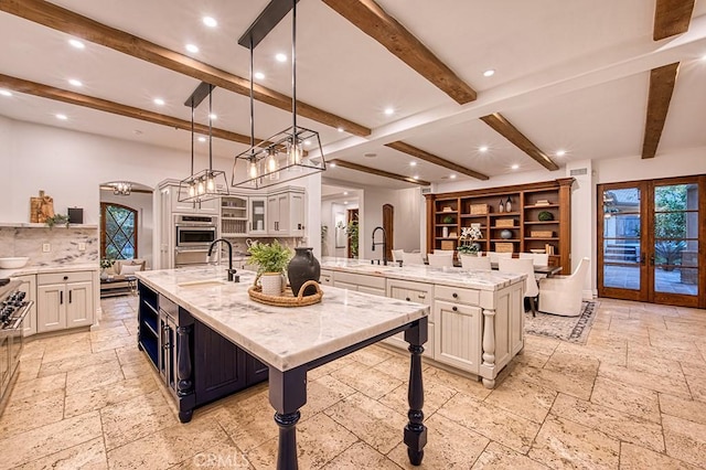 kitchen featuring pendant lighting, a large island, beam ceiling, and light stone counters