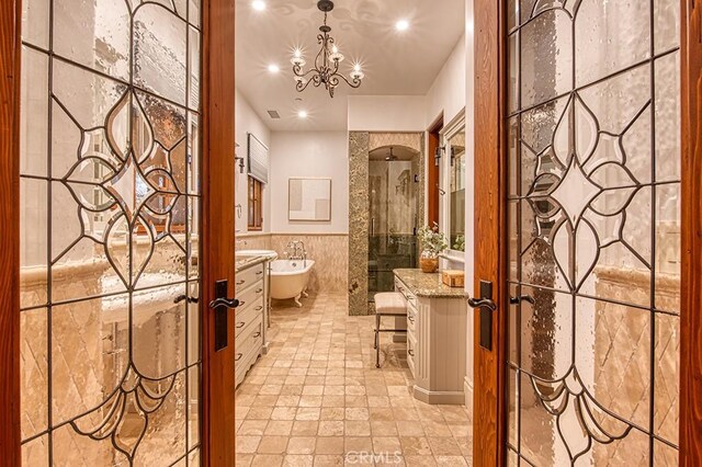 bathroom featuring vanity, a freestanding bath, a shower stall, tile walls, and a notable chandelier