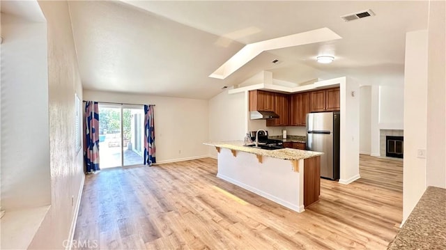 kitchen with kitchen peninsula, light wood-type flooring, stainless steel refrigerator, and a breakfast bar area