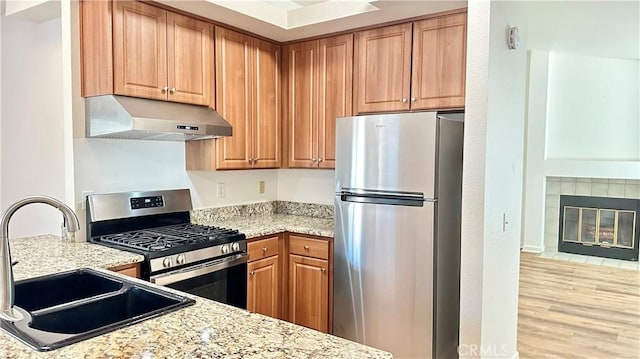 kitchen with light stone countertops, sink, appliances with stainless steel finishes, and a tile fireplace