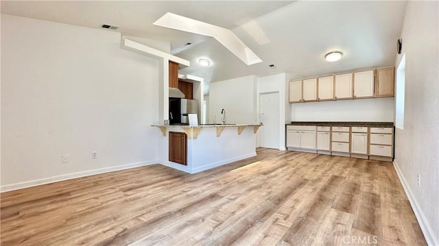 kitchen with a breakfast bar, kitchen peninsula, stainless steel refrigerator, sink, and light wood-type flooring