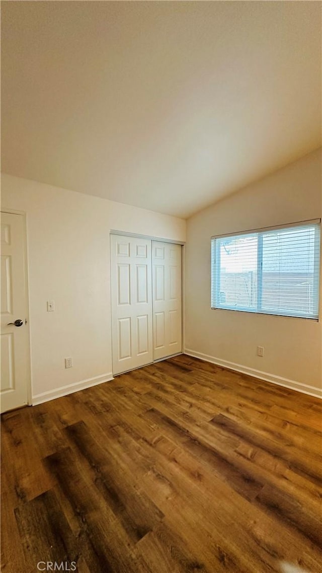 unfurnished bedroom featuring vaulted ceiling, dark wood-type flooring, and a closet