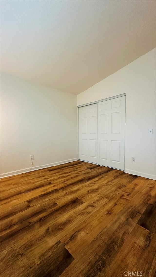 unfurnished bedroom with lofted ceiling, a closet, and dark wood-type flooring