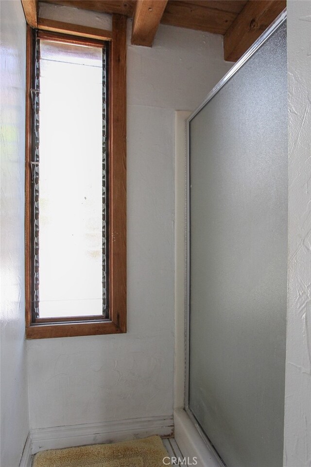 bathroom with beam ceiling and a shower with door