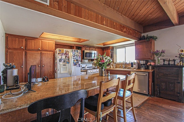 kitchen with a breakfast bar area, a sink, stainless steel appliances, wood finished floors, and brown cabinetry