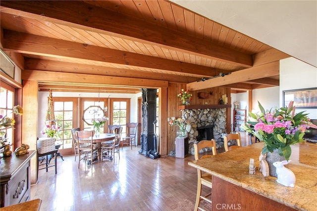 dining space with wooden ceiling, a stone fireplace, wood-type flooring, beam ceiling, and wooden walls