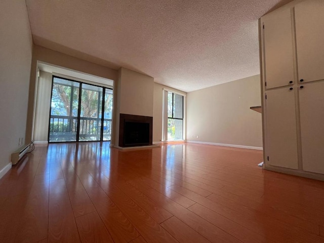 unfurnished living room with baseboard heating, a textured ceiling, and light wood-type flooring