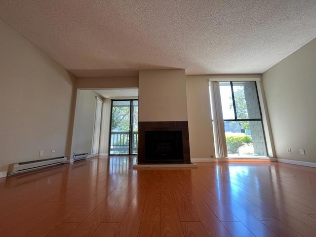 unfurnished living room with wood-type flooring, plenty of natural light, a baseboard heating unit, and a fireplace