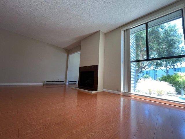 unfurnished living room featuring wood-type flooring, a fireplace, a textured ceiling, and a baseboard heating unit