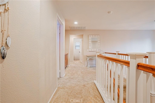 hallway with visible vents, a textured wall, light carpet, an upstairs landing, and baseboards