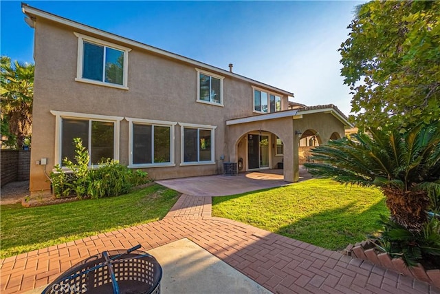 rear view of property featuring a lawn, a patio, and stucco siding