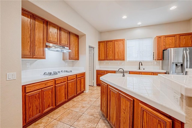 kitchen featuring brown cabinetry, stainless steel refrigerator with ice dispenser, white gas cooktop, and under cabinet range hood