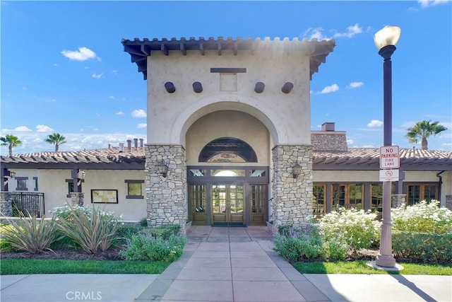 doorway to property with stucco siding, a tile roof, a chimney, and french doors