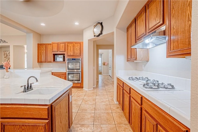 kitchen with stainless steel double oven, a sink, brown cabinetry, and under cabinet range hood