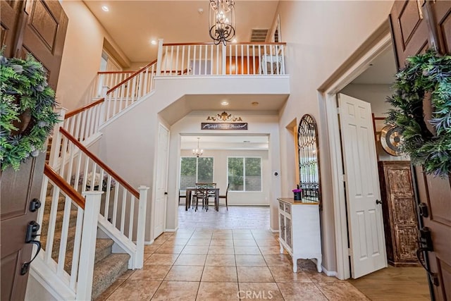 entrance foyer featuring stairs, light tile patterned floors, a towering ceiling, and an inviting chandelier