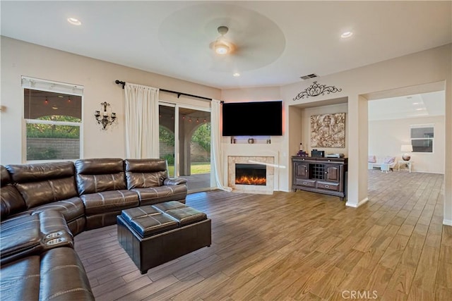 living room with a warm lit fireplace, baseboards, ceiling fan, light wood-type flooring, and recessed lighting