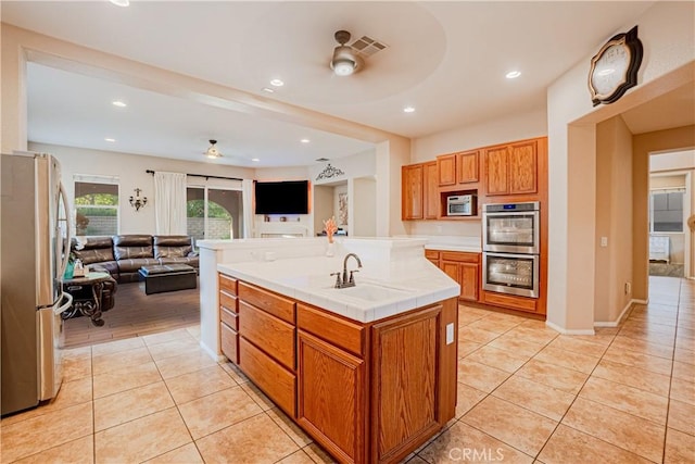 kitchen with light tile patterned floors, brown cabinets, open floor plan, stainless steel appliances, and a sink