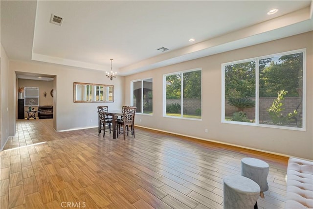 dining area with light wood finished floors, visible vents, radiator, a tray ceiling, and a chandelier