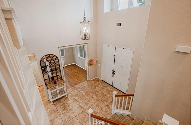 foyer entrance featuring light tile patterned floors, a towering ceiling, visible vents, stairway, and an inviting chandelier