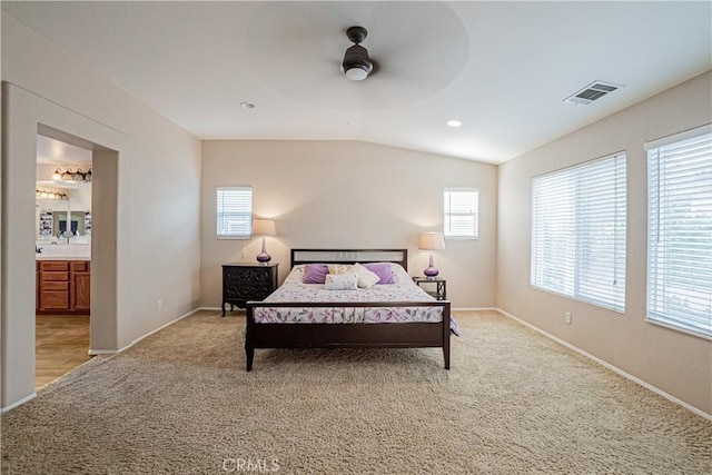 bedroom with lofted ceiling, light colored carpet, visible vents, ensuite bathroom, and baseboards