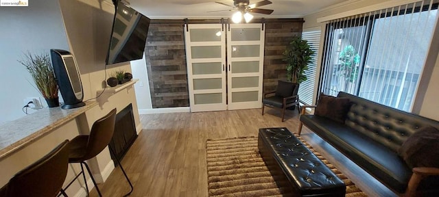 living room with light wood-type flooring, ceiling fan, a barn door, ornamental molding, and wood walls