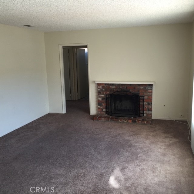 unfurnished living room featuring a textured ceiling, a brick fireplace, and dark carpet