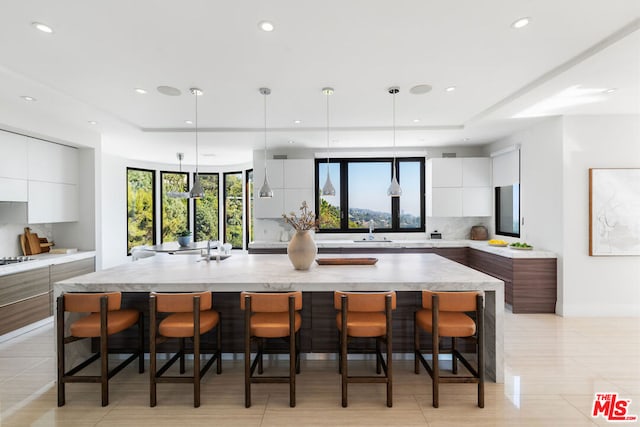 kitchen featuring pendant lighting, a breakfast bar, white cabinets, a spacious island, and tasteful backsplash