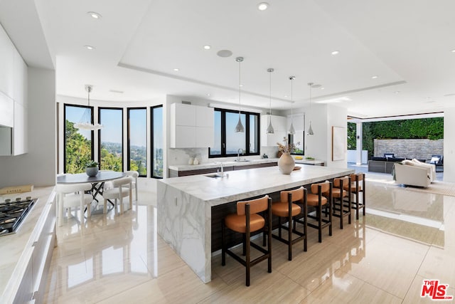 kitchen with hanging light fixtures, a kitchen breakfast bar, light stone counters, a large island with sink, and white cabinets