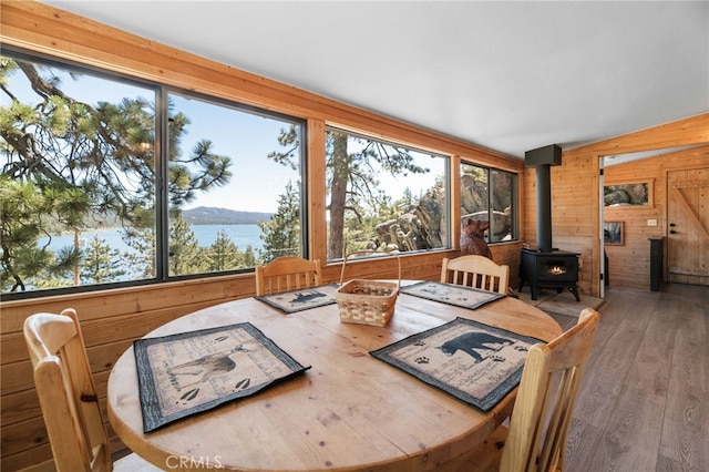 dining room featuring wood-type flooring, a water view, wood walls, and a wood stove