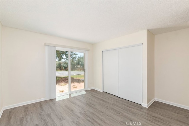 unfurnished bedroom with a closet, access to outside, hardwood / wood-style floors, and a textured ceiling