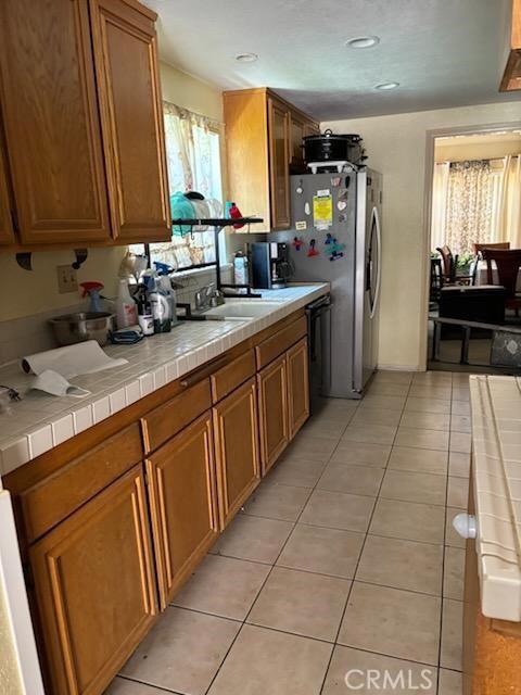 kitchen with tile countertops, dishwasher, light tile patterned floors, and sink