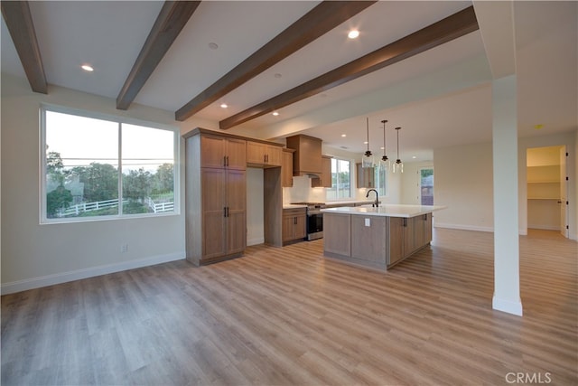 kitchen with light hardwood / wood-style flooring, decorative light fixtures, a kitchen island with sink, sink, and stainless steel range