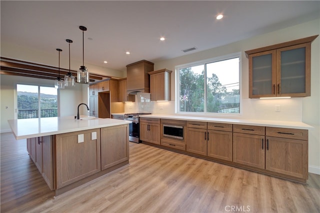 kitchen with tasteful backsplash, decorative light fixtures, a kitchen island with sink, stainless steel appliances, and light wood-type flooring