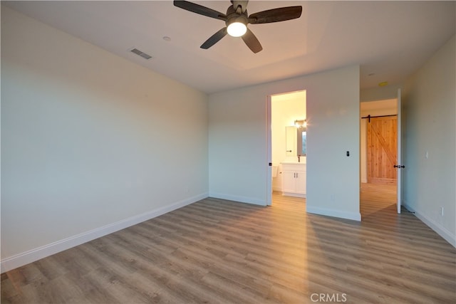 spare room featuring light hardwood / wood-style floors, ceiling fan, and a barn door