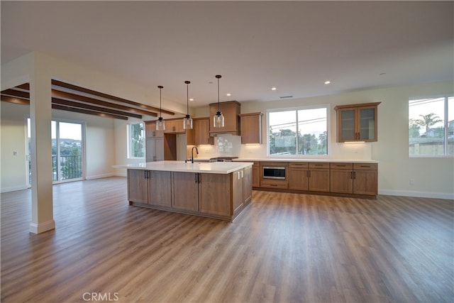 kitchen featuring hanging light fixtures, light hardwood / wood-style floors, stainless steel microwave, a kitchen island with sink, and sink