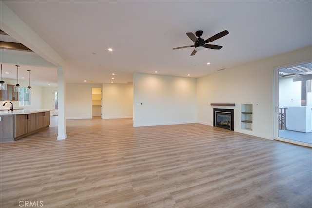 unfurnished living room with ceiling fan, light wood-type flooring, and sink