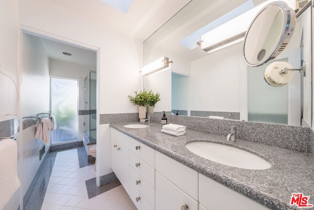 bathroom with a shower with door, toilet, a skylight, vanity, and tile patterned floors