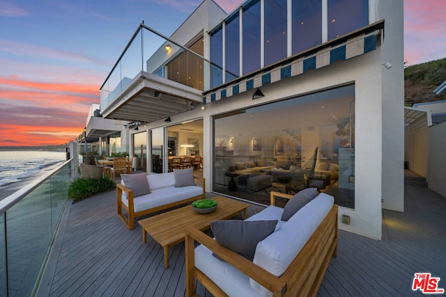 deck at dusk with outdoor lounge area and a water view