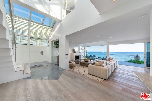 living room with a towering ceiling, a healthy amount of sunlight, a water view, and light wood-type flooring