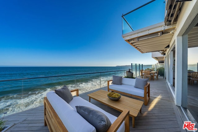 wooden terrace featuring outdoor lounge area, a water view, and a beach view