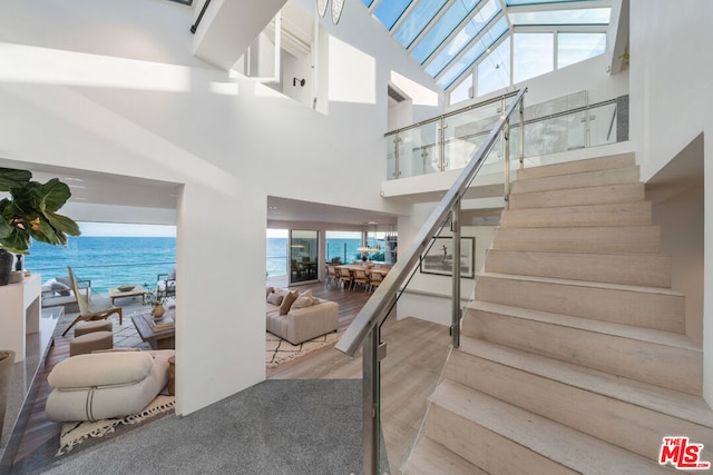 stairs featuring plenty of natural light, hardwood / wood-style floors, high vaulted ceiling, and a water view