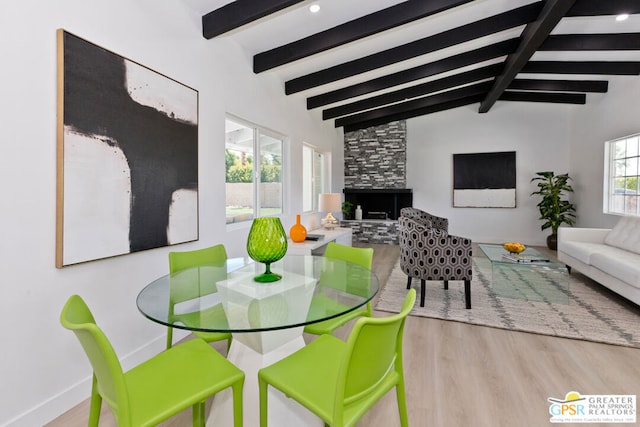 dining room with hardwood / wood-style flooring, lofted ceiling with beams, and a stone fireplace