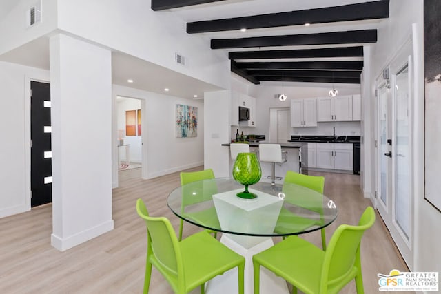 dining area featuring light wood-type flooring, lofted ceiling with beams, and sink