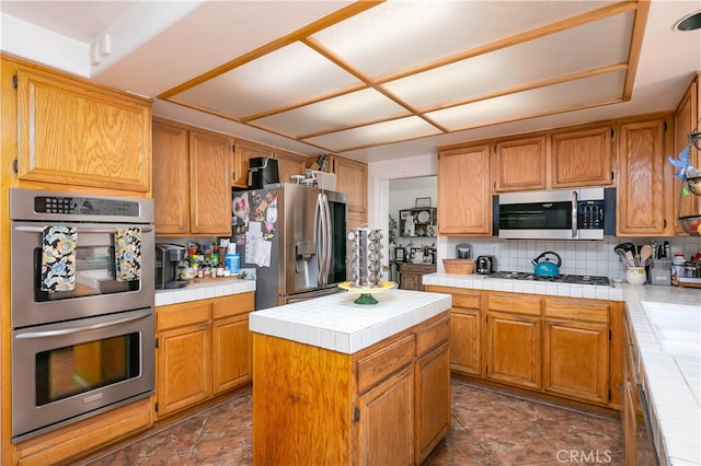 kitchen featuring backsplash, appliances with stainless steel finishes, tile countertops, and a kitchen island