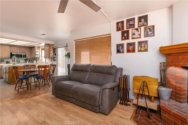 living room featuring ceiling fan, light hardwood / wood-style flooring, and a fireplace