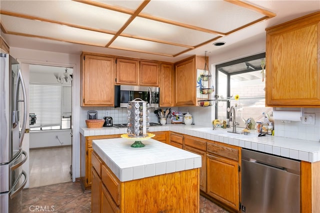 kitchen with tasteful backsplash, a kitchen island, stainless steel appliances, tile counters, and sink