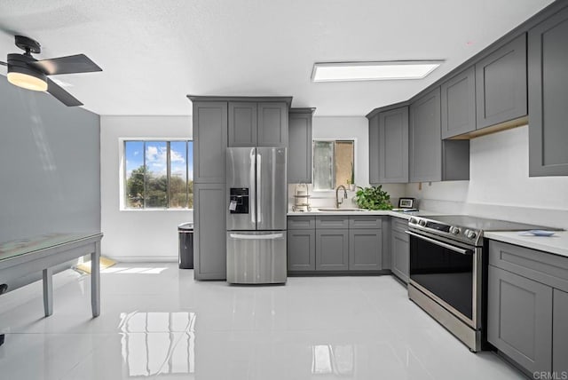 kitchen with gray cabinetry, light tile patterned flooring, stainless steel appliances, ceiling fan, and sink